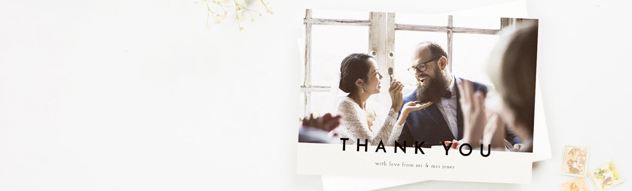 A printed wedding thank you card showing a married couple eating their wedding cake. The card reads “Thank You”